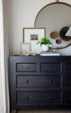 a dresser with a mirror, plant and pictures on it