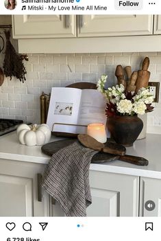 an open book sitting on top of a counter next to a candle and some flowers