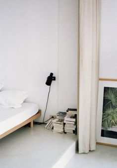 a bed sitting next to a stack of books on top of a white floor near a window