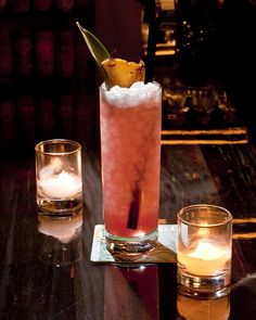 a tall glass filled with a drink next to two candles