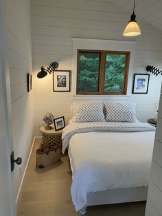 a white bed sitting under a window next to a night stand with pictures on it