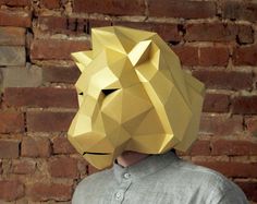 a man wearing a paper lion mask in front of a brick wall