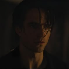 a man with dark hair and blue eyes stares into the distance in a dimly lit room