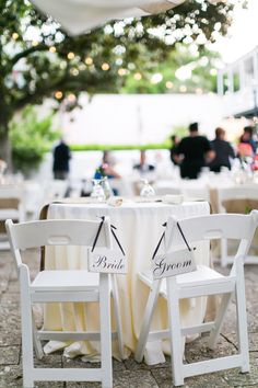 two white chairs sitting next to each other on top of a stone floor covered ground