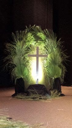 a cross is lit up in the middle of a room with grass growing around it