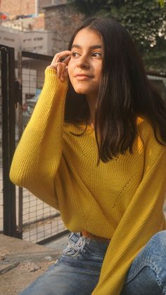 a woman sitting on the ground with her hand to her ear and looking off into the distance