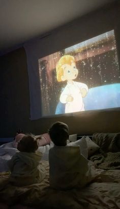 two small children sitting on a bed watching a movie in front of a large screen