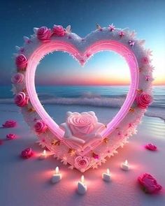 a heart shaped frame with roses and candles in the sand at sunset on a beach