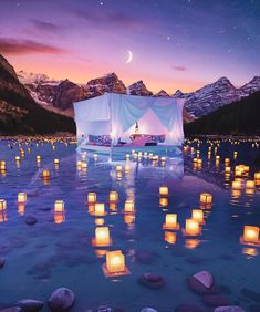 lanterns floating in the water with a tent on it and mountains in the background at night