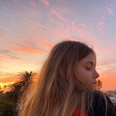 a woman with long blonde hair standing in front of the sky at sunset, looking off into the distance