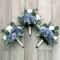 three bridal bouquets with blue and white flowers are arranged on a wood floor