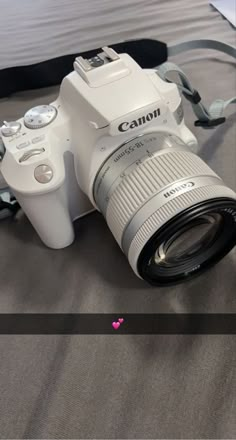 a white camera sitting on top of a bed next to a black and white bag