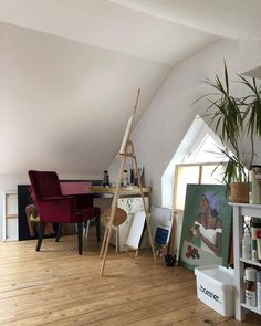 a room with white walls and wooden floors has a red chair in the corner next to an easel