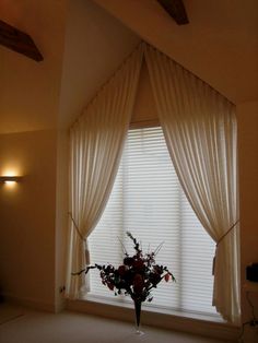 a vase filled with flowers sitting in front of a window covered in white drapes