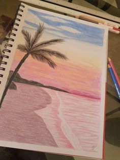 a drawing of a palm tree on the beach with watercolor pencils next to it