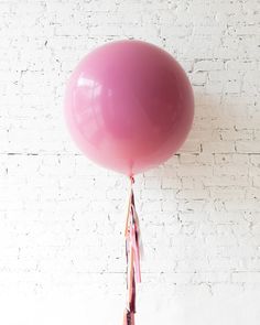 a pink balloon with tassels hanging from it's side against a white brick wall