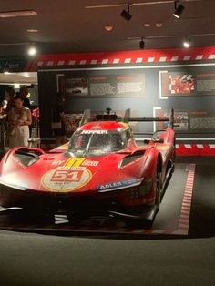 a red race car on display in a museum with people looking at the cars behind it