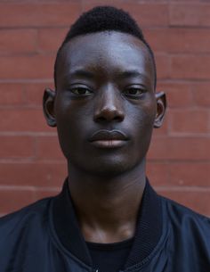 a young man in front of a brick wall looking at the camera with an intense look on his face