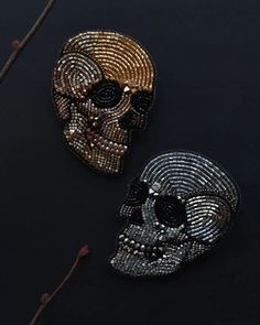 two beaded skulls sitting next to each other on a black surface with one skull in the middle