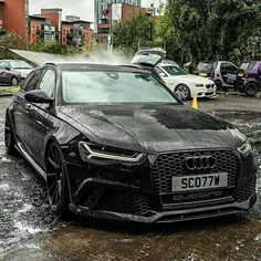 a black car is parked in the mud with other cars behind it and some buildings