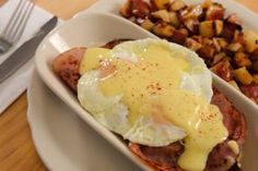 an egg on top of ham and potatoes in a white dish next to a fork