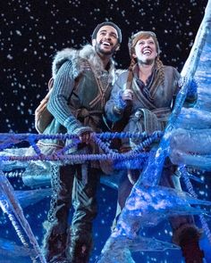 two men dressed in winter clothes standing next to each other on stage with snow falling all around them