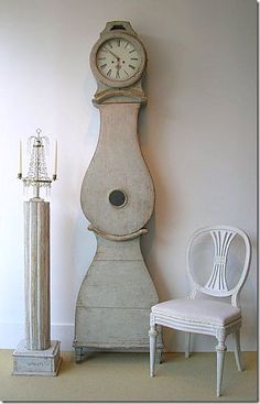 an old grandfather clock sitting next to a white chair and light pole in a room