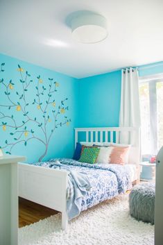 a bedroom painted in blue and white with a tree mural on the wall above the bed