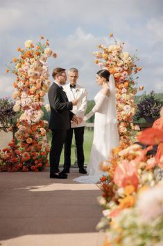 a bride and groom standing in front of an arch with flowers