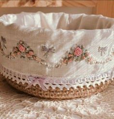 a crocheted basket with pink flowers on it sitting on a doily covered bed