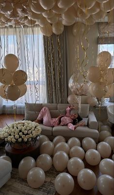 a living room filled with lots of balloons and white flowers on top of a wooden floor