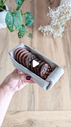 a person holding a tray with cookies in it on top of a wooden table next to a potted plant