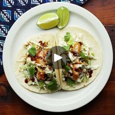 two fish tacos on a white plate with lime wedges