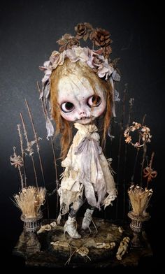 a creepy looking doll sitting on top of a pile of dead flowers and plants with eyes wide open