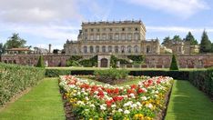 a large building with lots of flowers in front of it and hedges around the perimeter