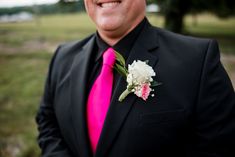 a man in a black suit with a pink tie and flower boutonniere