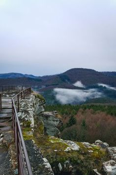 a wooden walkway on top of a cliff with mountains in the background and foggy sky