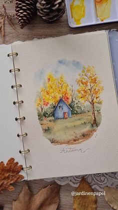 an open notebook with watercolors and autumn leaves