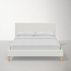 a bed with white sheets and pillows on top of the headboard, sitting in front of a wall