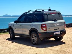 the back end of a silver truck parked on top of a dirt field next to water