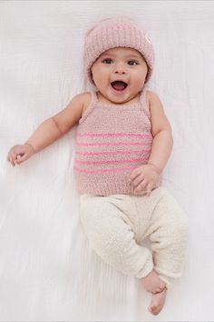 a baby is laying down wearing a pink hat and striped shirt with white pants on it