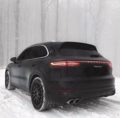 the rear end of a black porsche cayenne parked on snow covered ground in front of trees