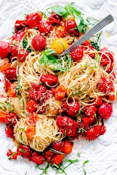 a white plate topped with pasta and cherry tomatoes next to a fork on top of it