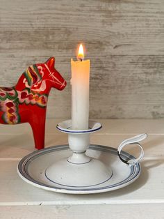 a white candle sitting on top of a metal plate next to a red horse figurine