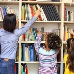 two girls reaching up to reach books on a book shelf in front of a library full of books