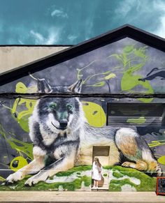 a painting of a wolf on the side of a building with a woman standing next to it