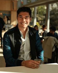 a man sitting at a table with a drink in his hand and smiling for the camera