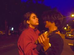 two people standing next to each other in the street at night with their arms around each other