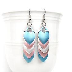 "Lightweight anodized aluminum scales cascade over one another in these stunning transgender pride chainmail earrings. There is one scale of each color of the 5 stripe flag: light blue, light pink, white, light pink, and light blue. The gorgeous scales have a subtle shimmer and are anodized on both sides as well as the edges. Silver aluminum jump rings link the scales.  Including the French hook ear wire, the earrings measure 2-3/4\" in length. They are just over 1/2\" wide. Dimes shown for scale. The current ear wires are hypoallergenic surgical stainless steel French hooks, but can be changed to steel lever backs if you prefer. Please select your ear wire preference from the drop down menu. See more trans jewelry here: https://www.etsy.com/shop/TattooedAndChained?search_query=transgender Chainmail Earrings, Trans Pride Flag, White Jewelry Box, Chain Maille Jewelry, Trans Pride, Hard Metal, White Jewelry, Pride Flag, Chain Mail