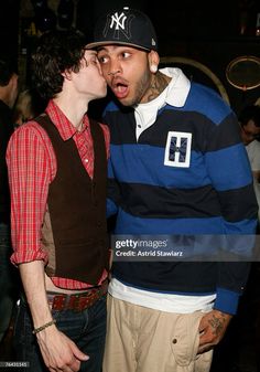 two men standing next to each other in front of a crowd at a party, one is kissing the other's cheek